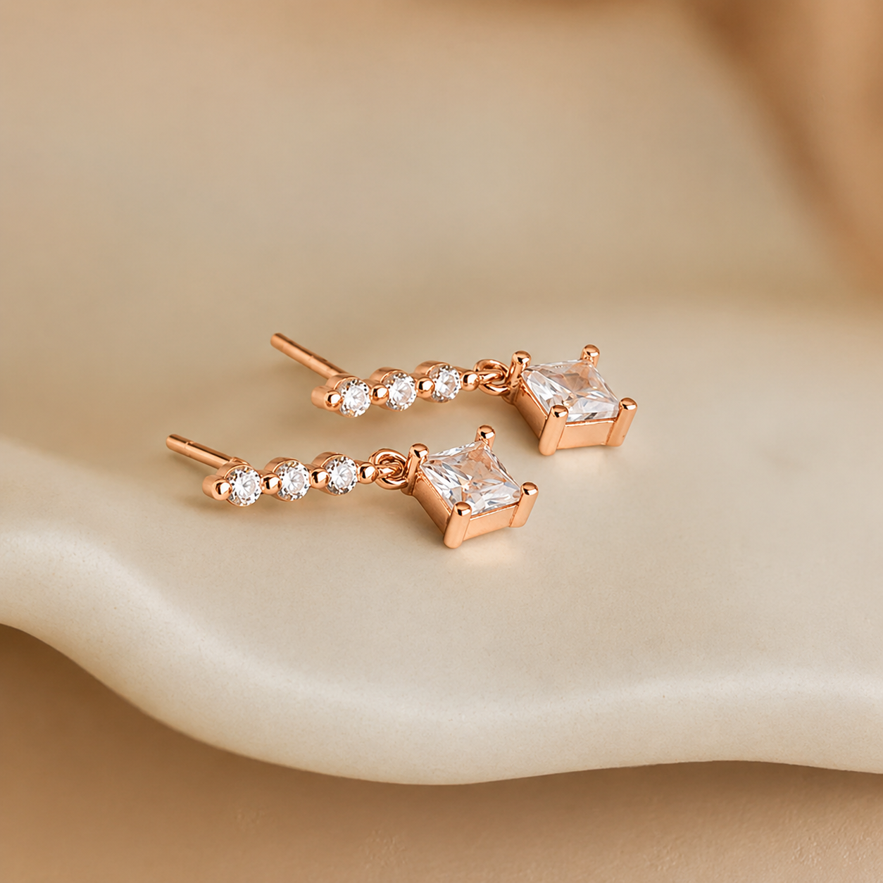 Rose gold earrings with clear gemstones on a beige surface