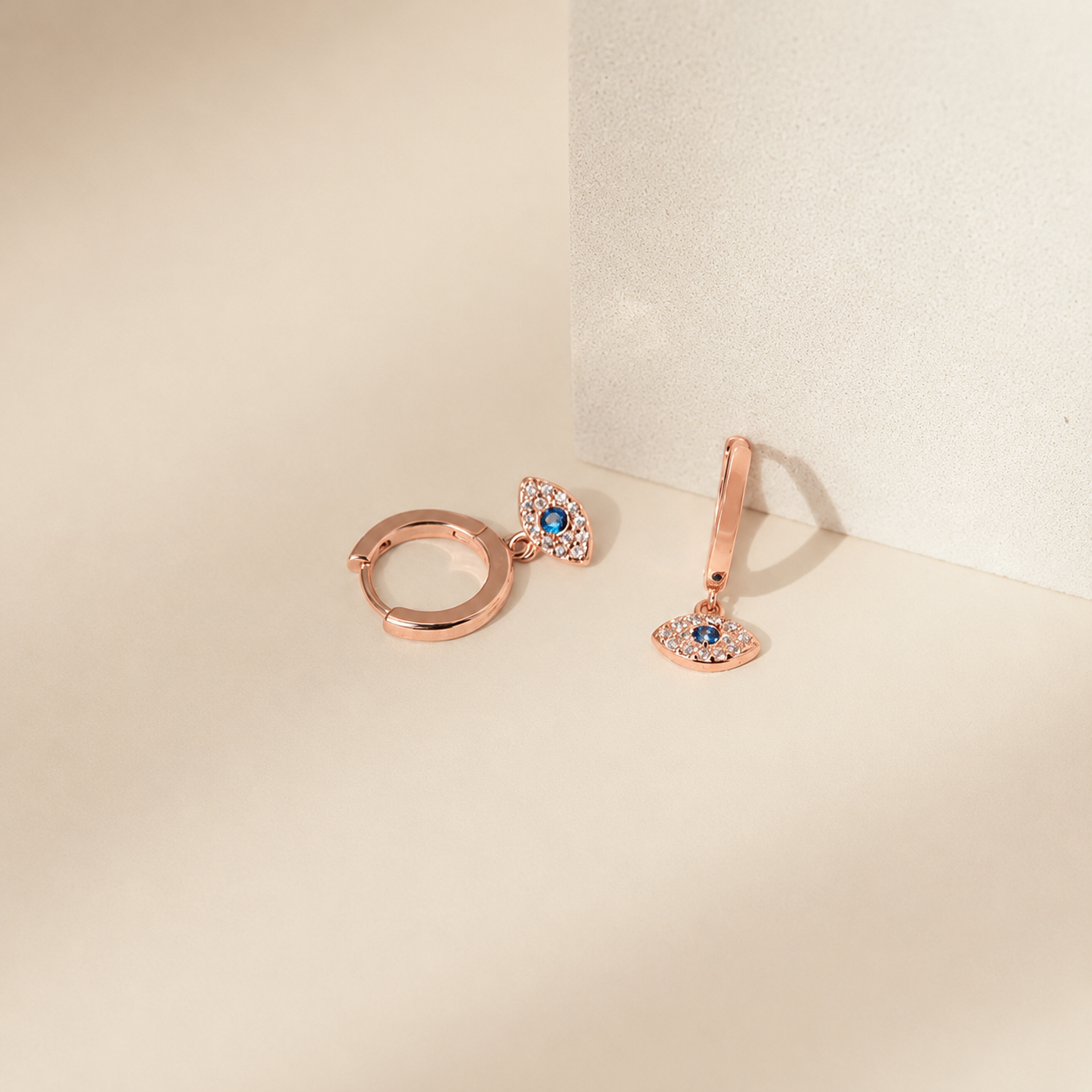 Rose gold hoop earrings with gemstones on a beige background