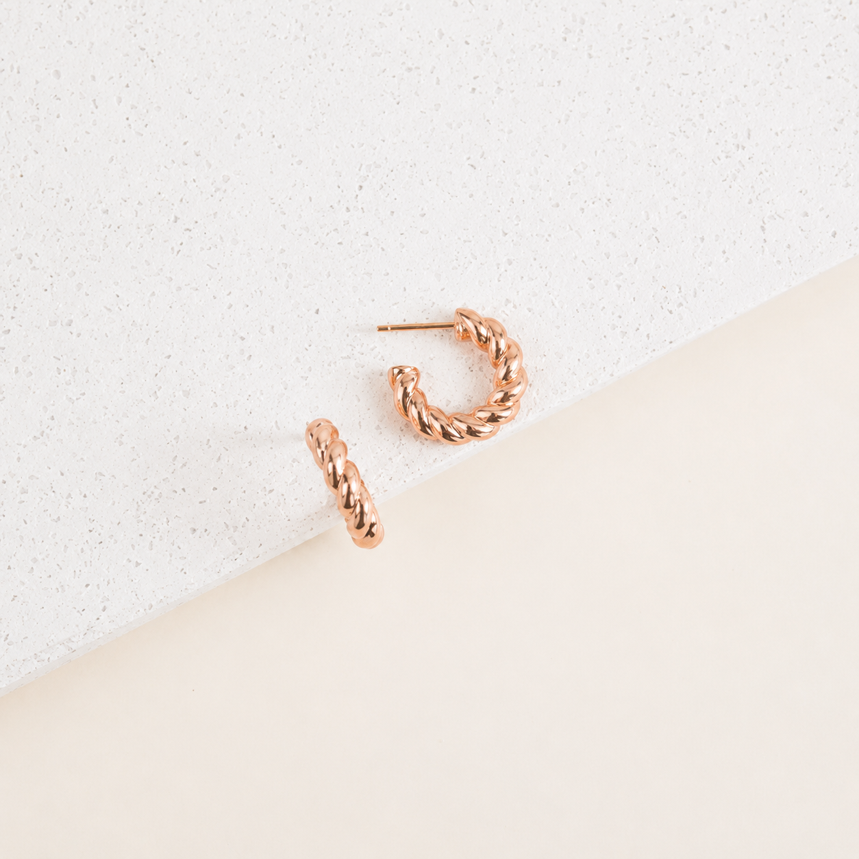 Rose gold hoop earrings on a textured white surface