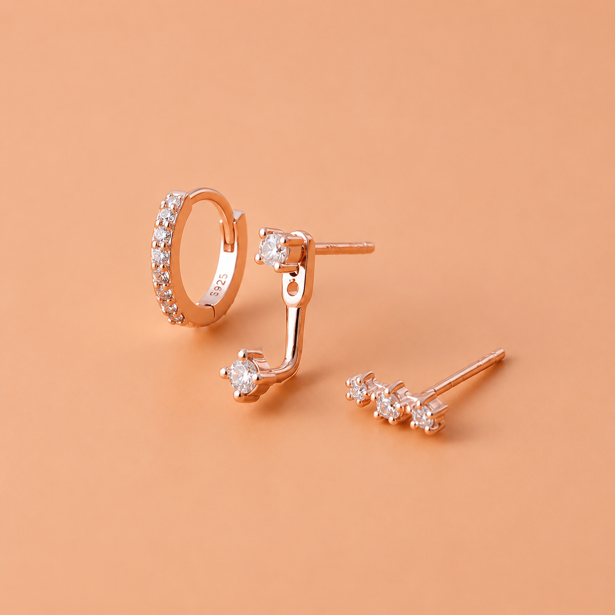 Rose gold hoop and stud earrings on a peach background