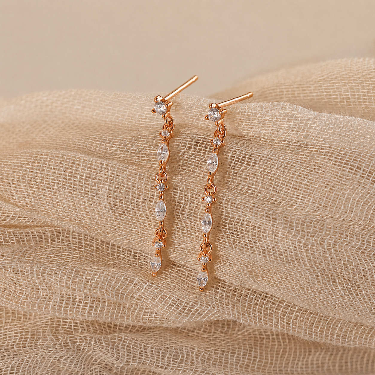 Rose gold earrings with clear stones on a beige fabric background