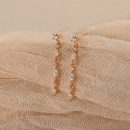 Rose gold earrings with clear stones on a beige fabric background