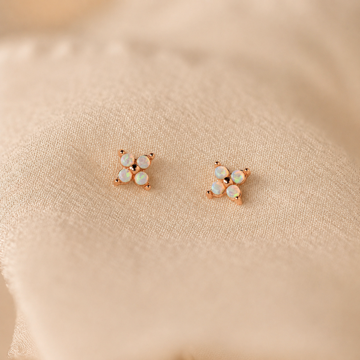 Pair of rose gold earrings with opal stones on a beige fabric background