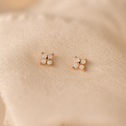 Pair of rose gold earrings with opal stones on a beige fabric background