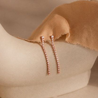 Rose gold earrings with small diamonds on a beige fabric background