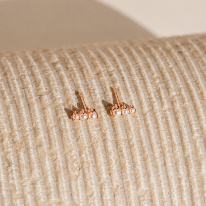 Rose gold earrings with pearls on a textured beige surface
