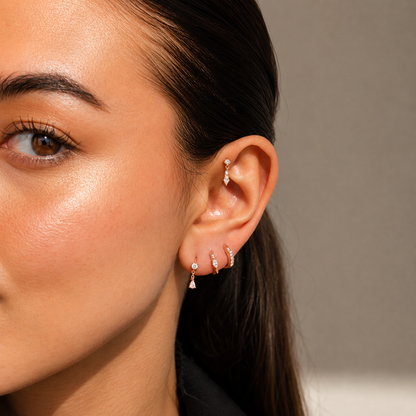 Close-up of a woman's ear with multiple earrings against a neutral background