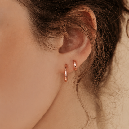 Close-up of a person wearing rose gold hoop earrings with a blurred background