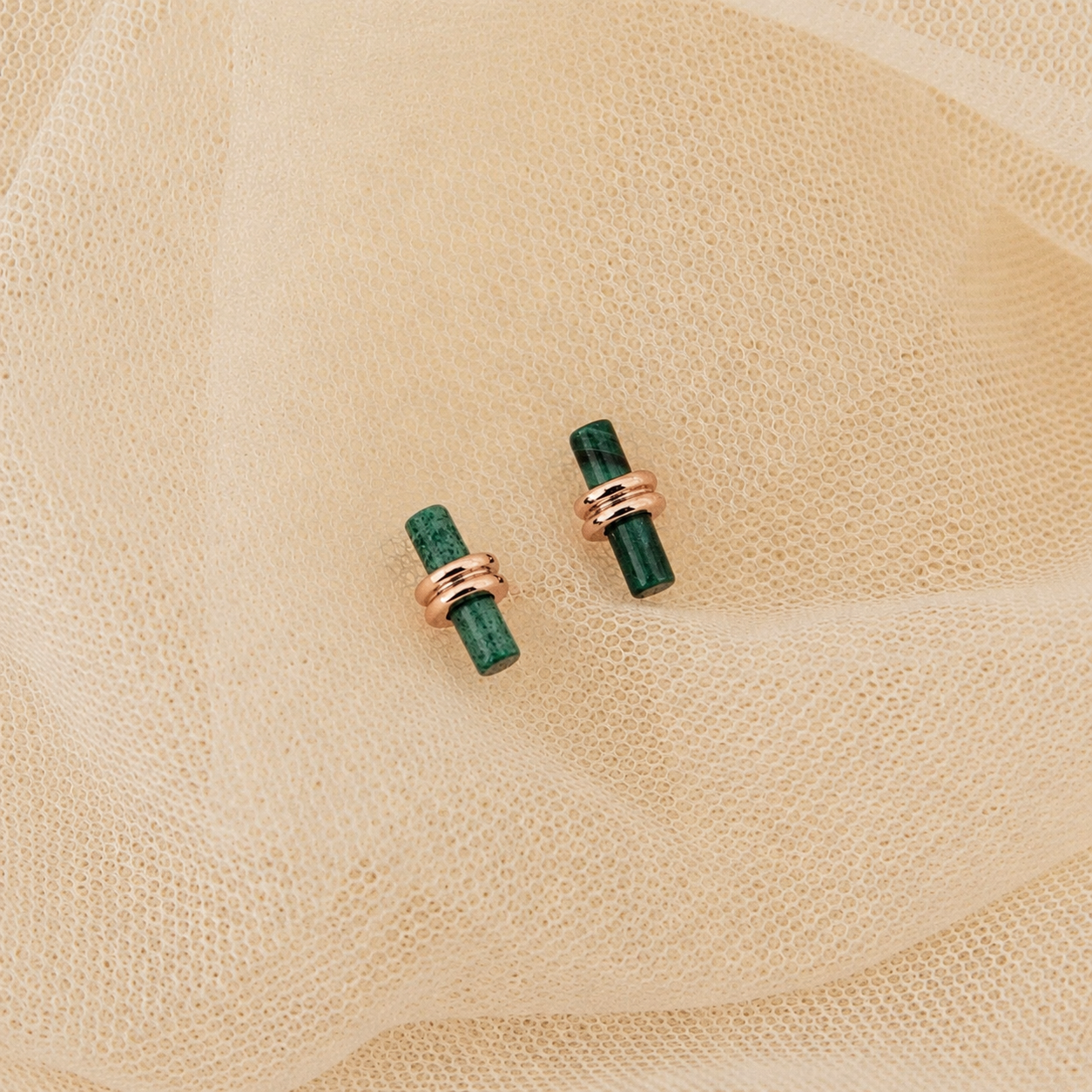Pair of green earrings with rose gold accents on a beige fabric background