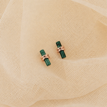 Pair of green earrings with rose gold accents on a beige fabric background