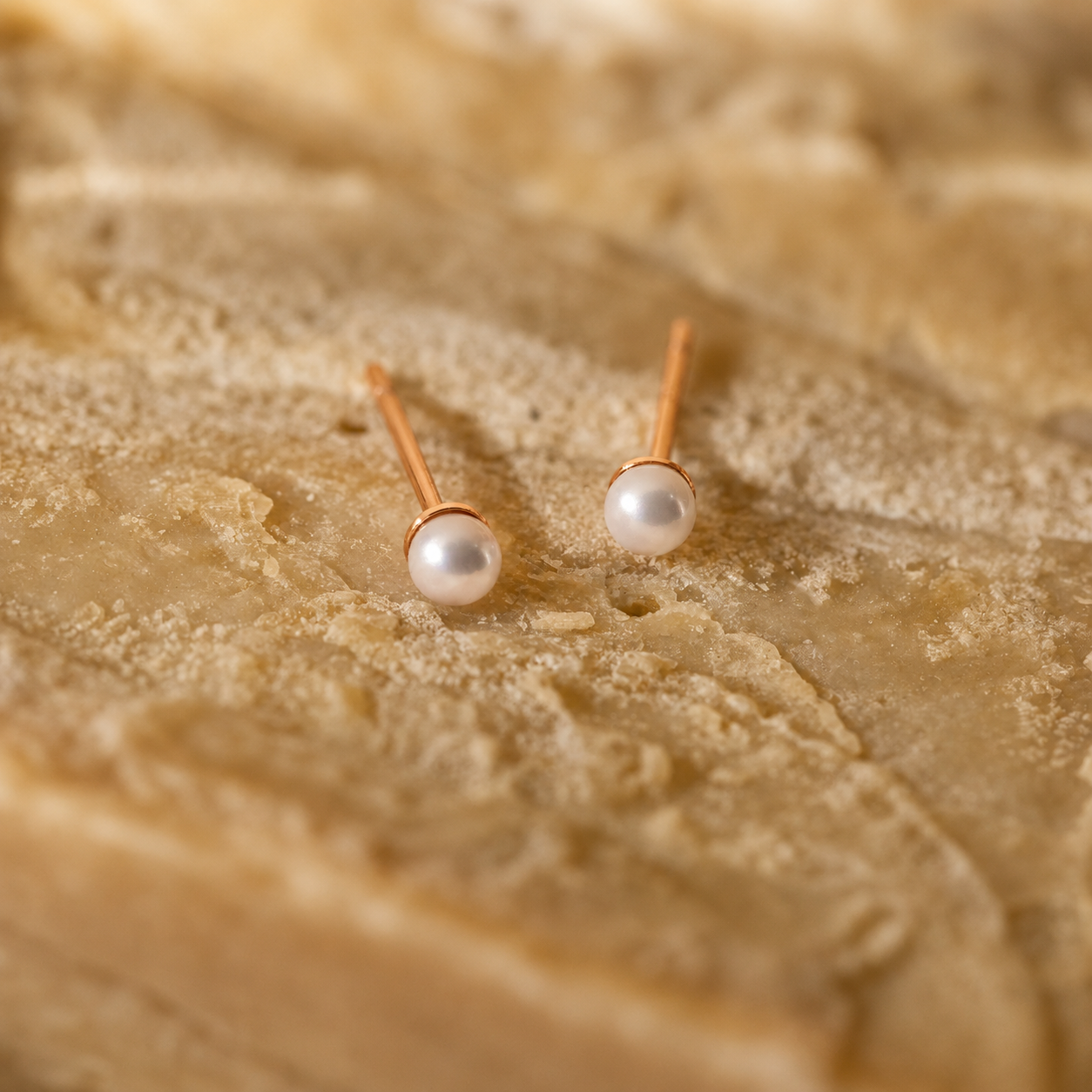 Pearl stud earrings on a textured beige surface