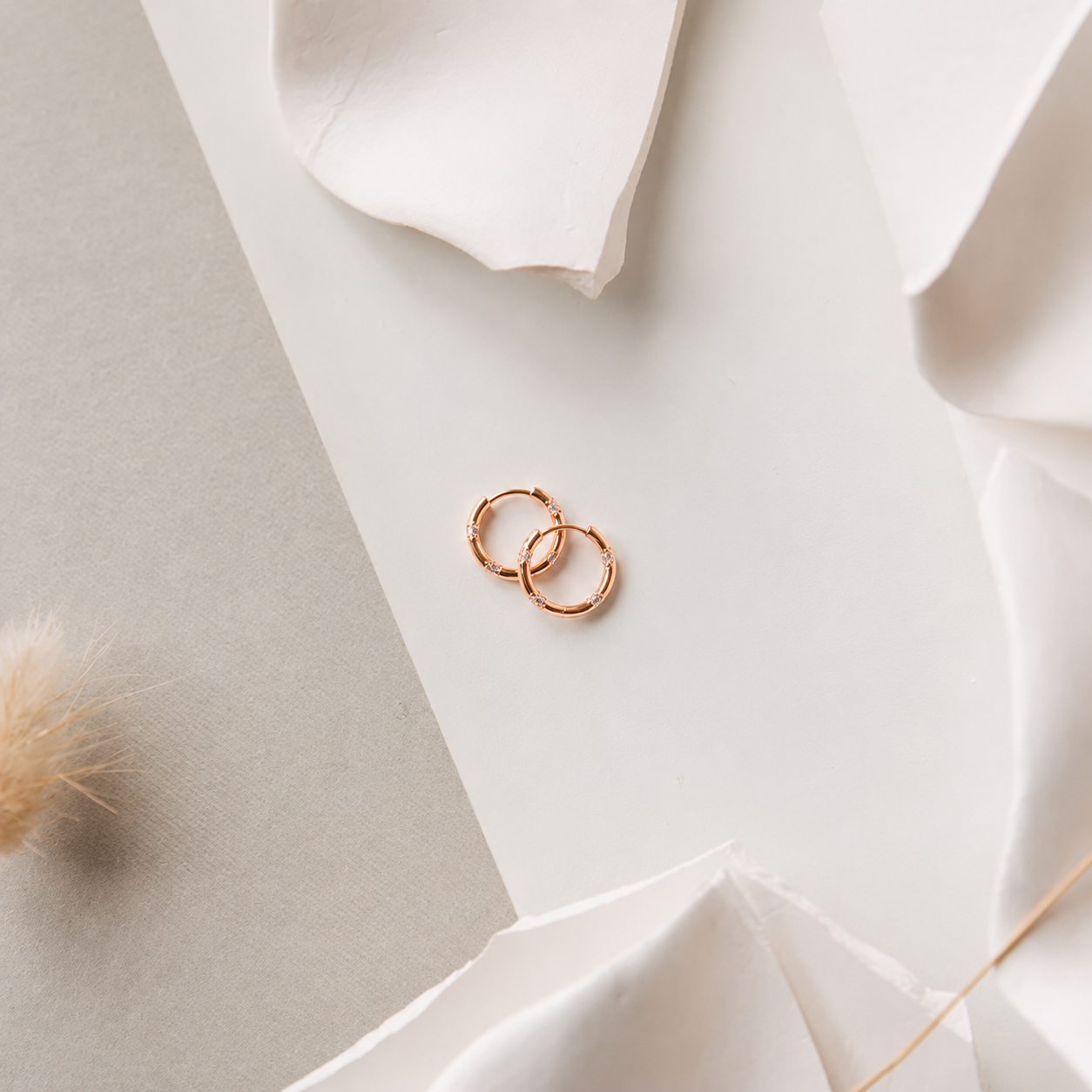 Two gold earring on a white fabric surface
