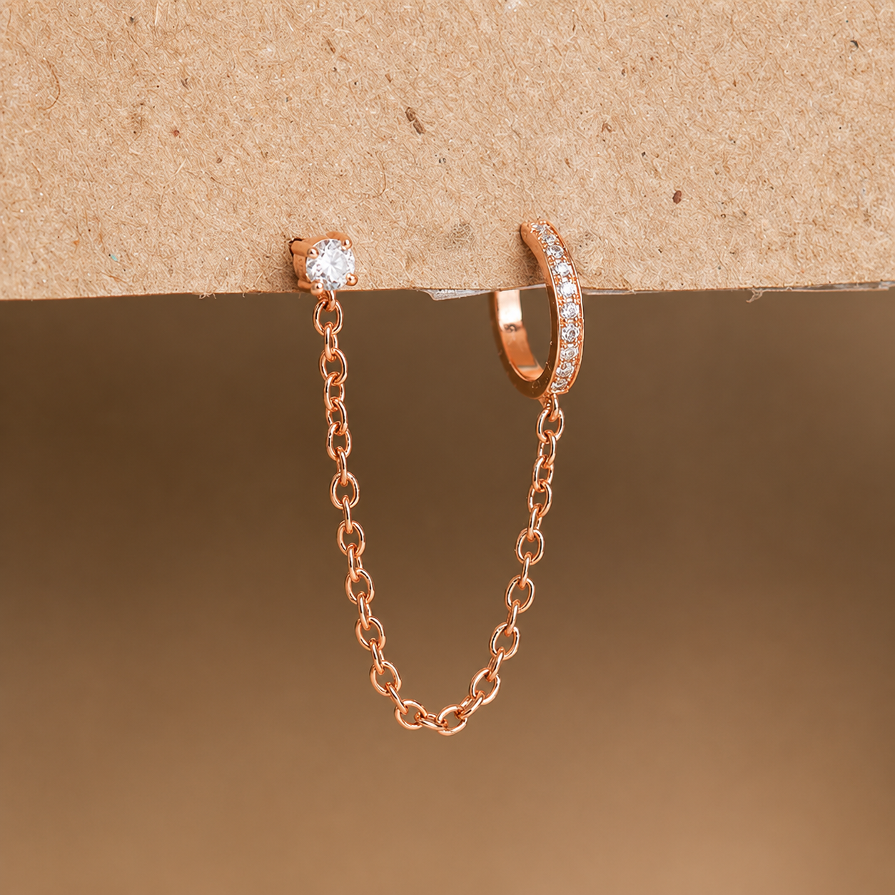 Rose gold chain earring and hoop earring on a brown background