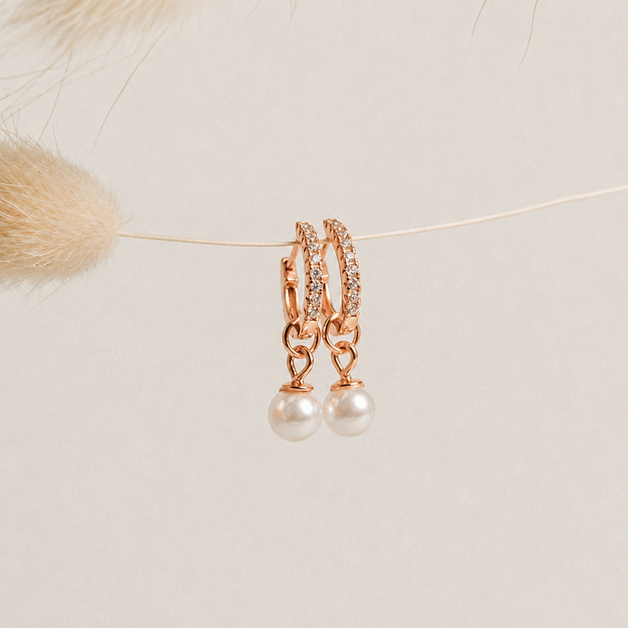 Rose gold hoop earrings with pearl drops on a neutral background