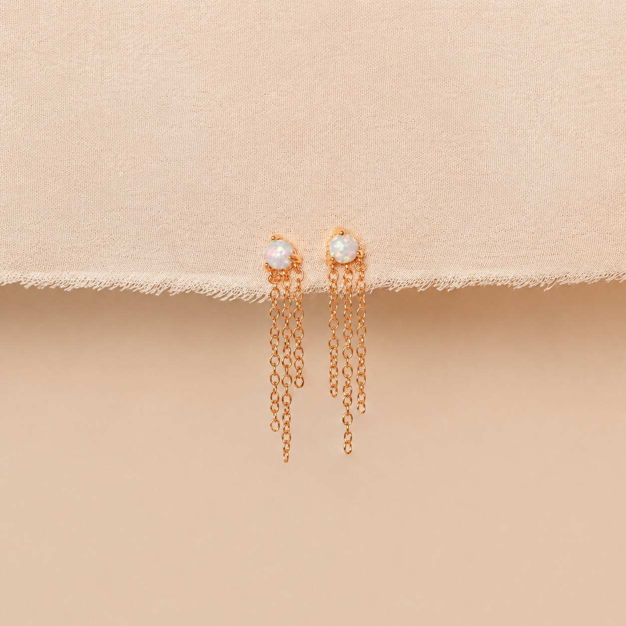 Gold chain earrings with pearl drops on a beige background