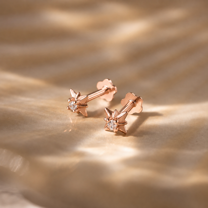 Rose gold earrings with small diamonds on a textured gold surface