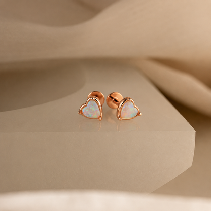 Rose gold heart-shaped opal earrings on a beige background