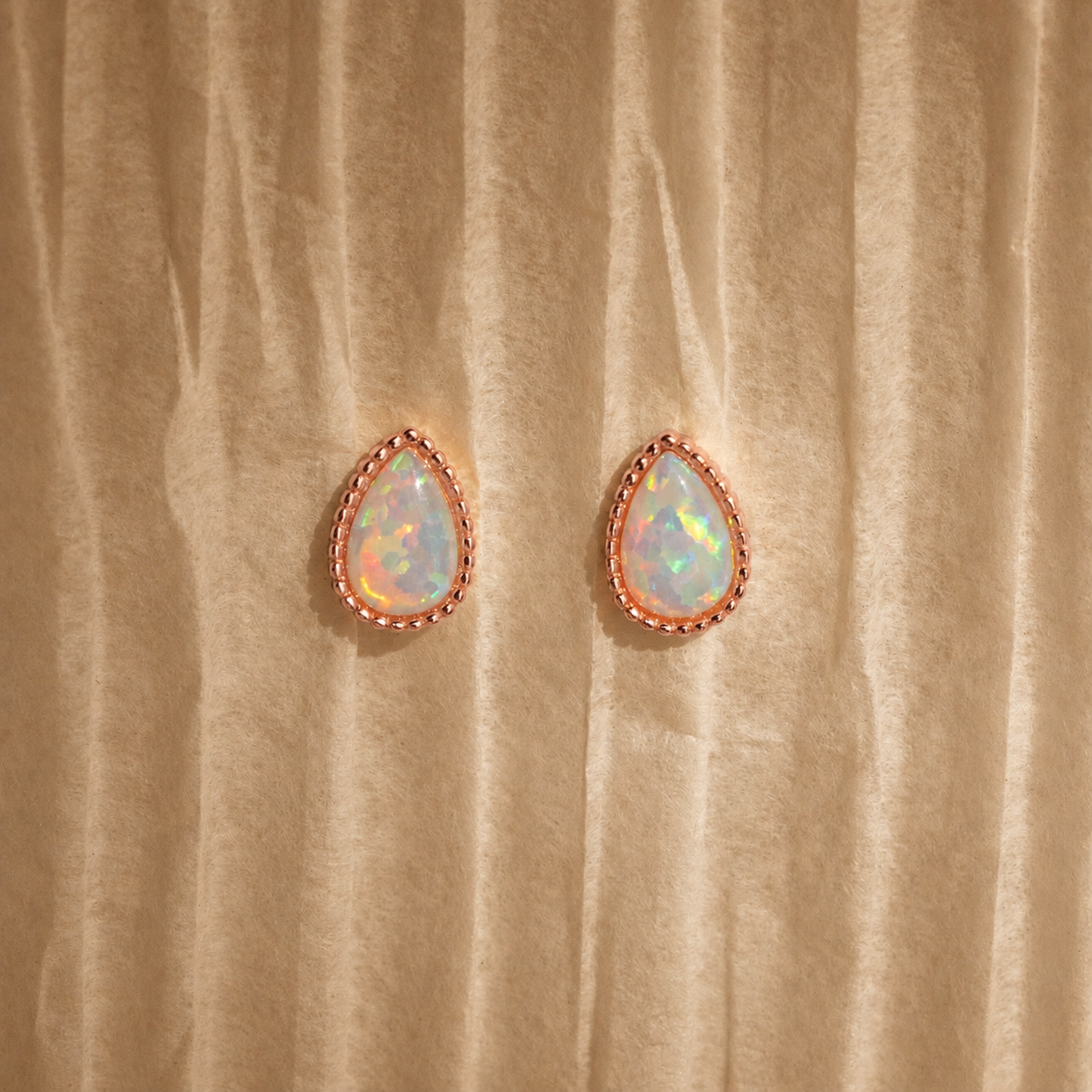 Teardrop-shaped opal earrings with rose gold setting on beige fabric background