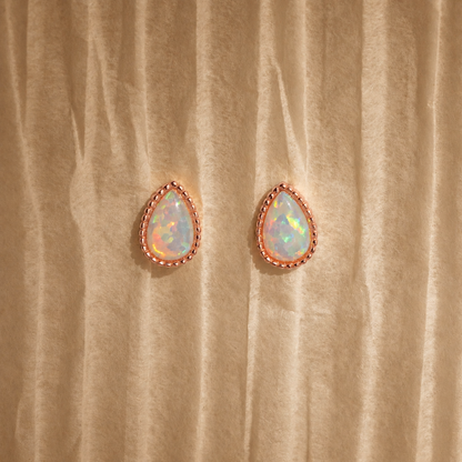 Teardrop-shaped opal earrings with rose gold setting on beige fabric background