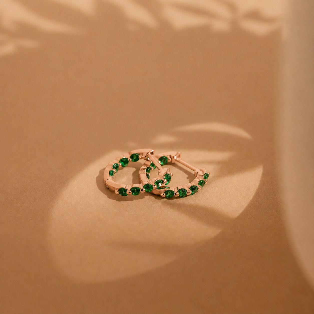Two gold hoop earrings with green gemstones on a beige background