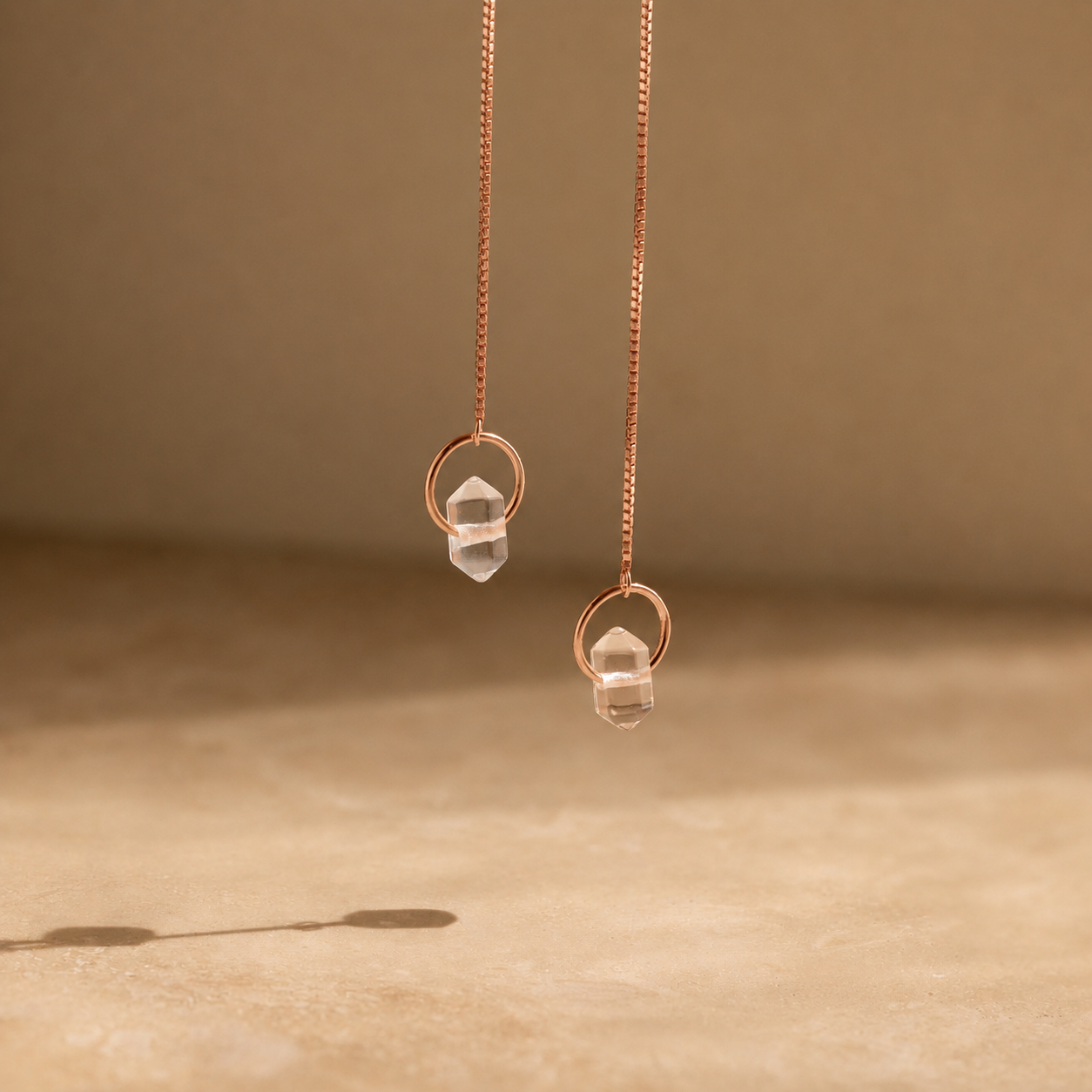 Rose gold earrings with clear gemstones on a beige background