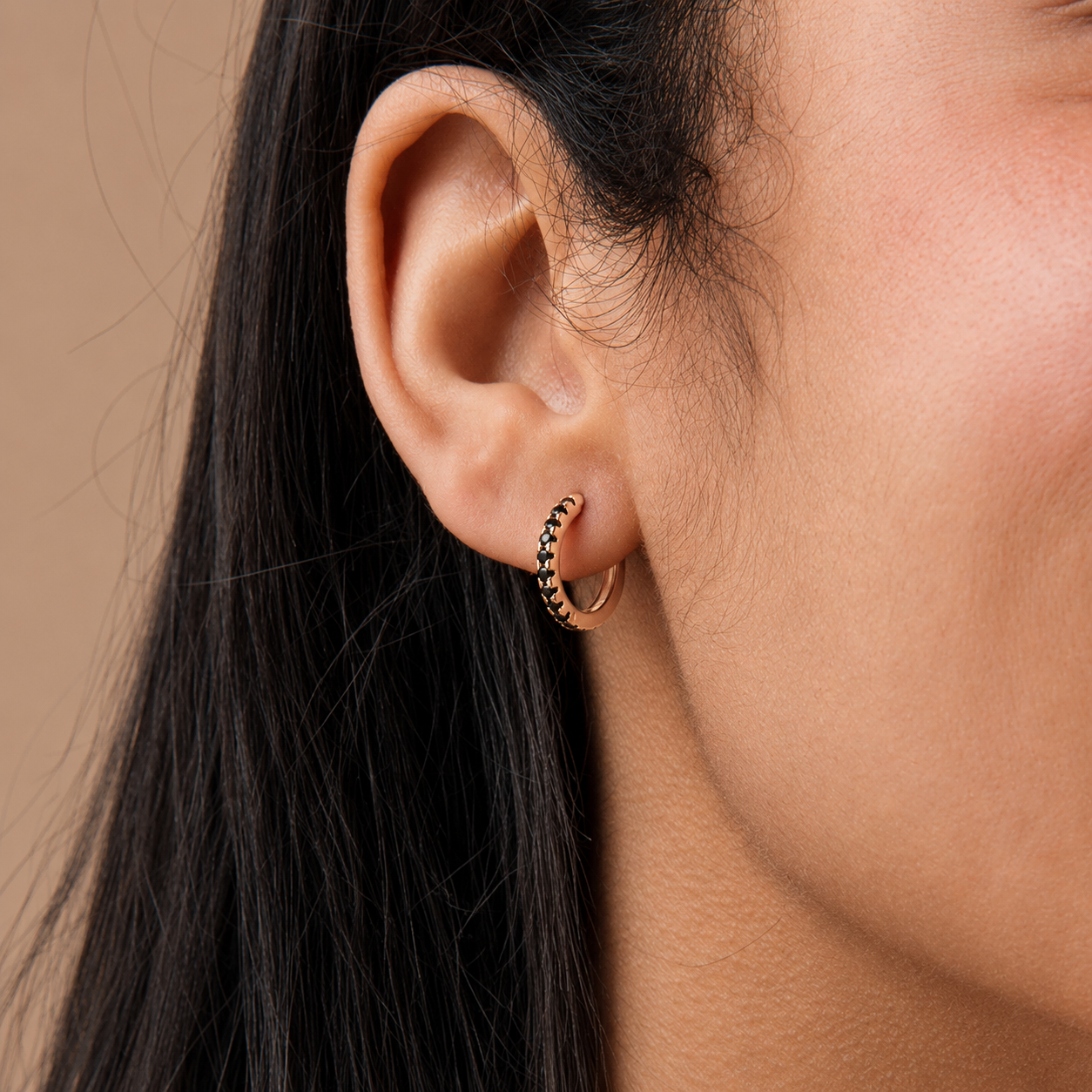 Close-up of an ear wearing a gold hoop earring with black accents on a neutral background