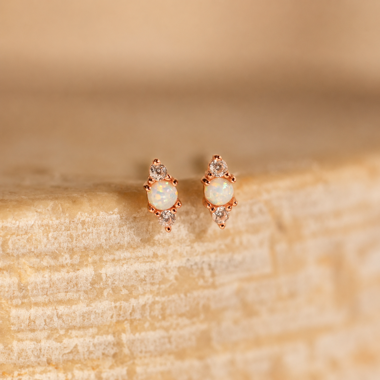 Pair of opal earrings with rose gold setting on a beige stone surface