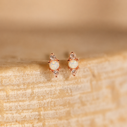 Pair of opal earrings with rose gold setting on a beige stone surface