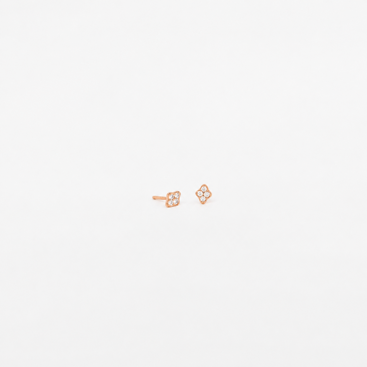 A pair of small rose gold stud earrings with a four-petal flower design set with tiny clear stones, shown on a plain white background.