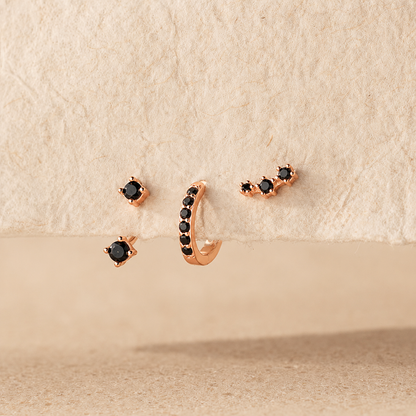 Rose gold earrings with black gemstones on a beige surface