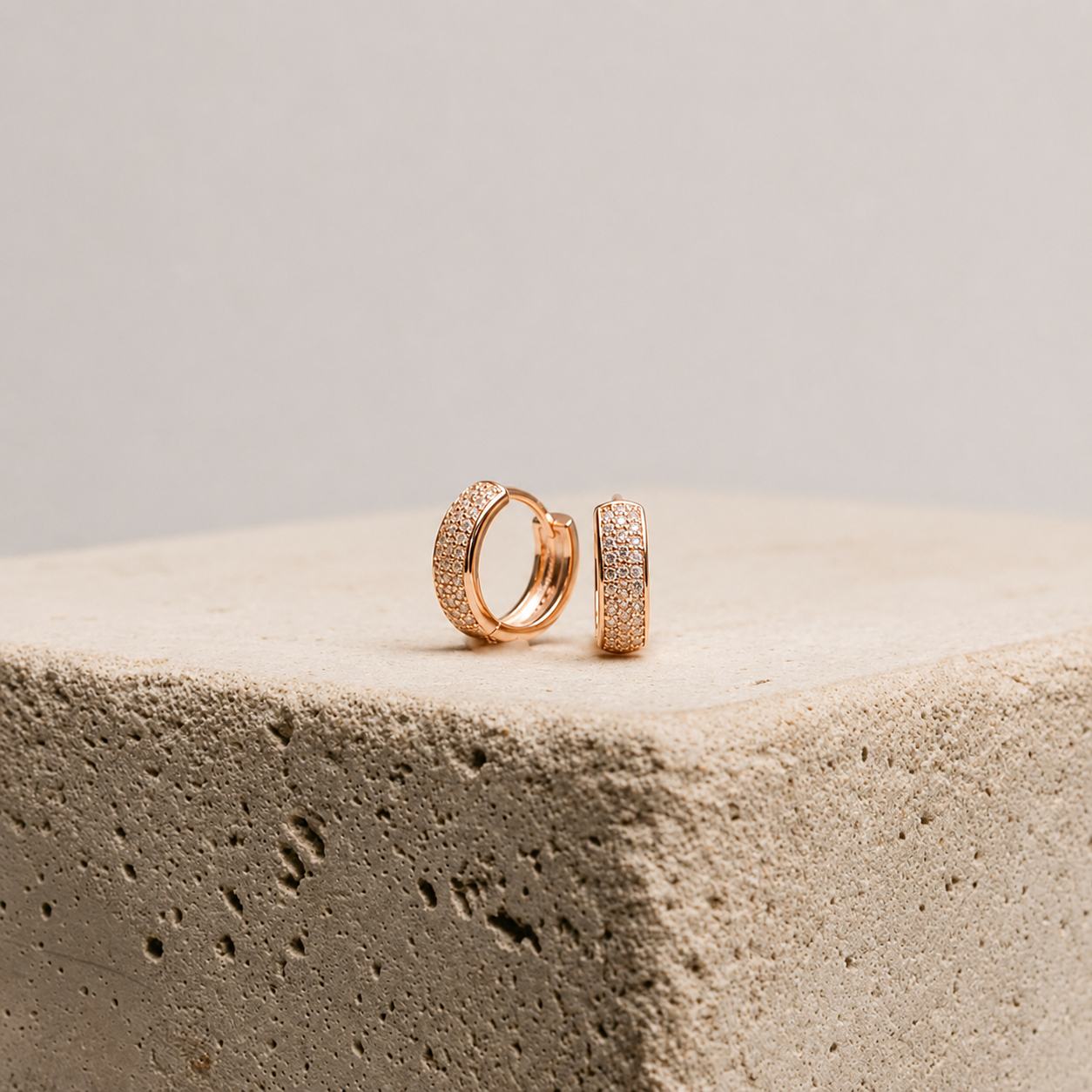 Rose gold hoop earrings on a textured beige surface with a neutral background
