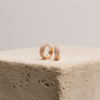 Rose gold hoop earrings on a textured beige surface with a neutral background