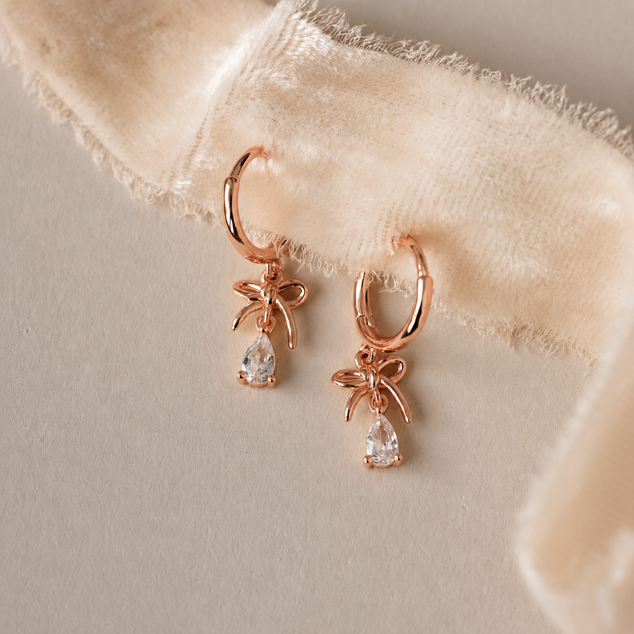 Rose gold hoop earrings with teardrop-shaped gemstones on a beige fabric background
