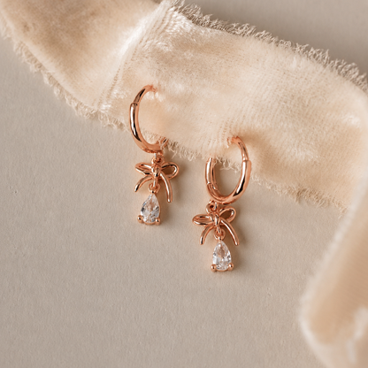 Rose gold hoop earrings with teardrop-shaped gemstones on a beige fabric background
