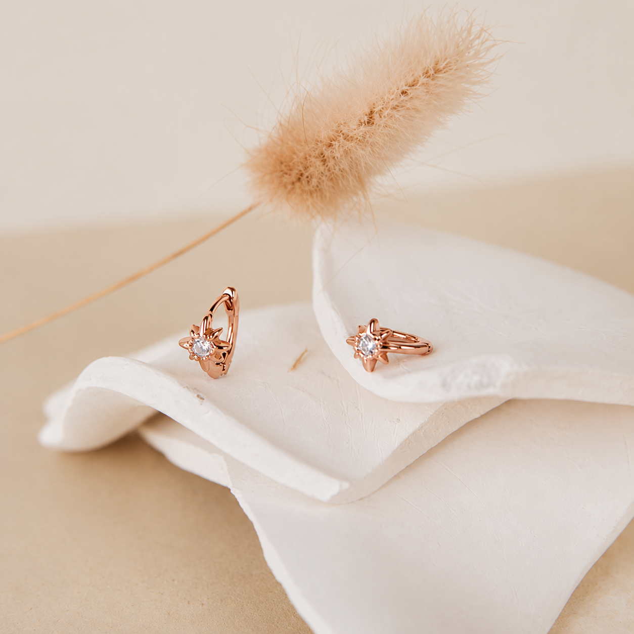 Rose gold hoop earrings on a white fabric with a beige background