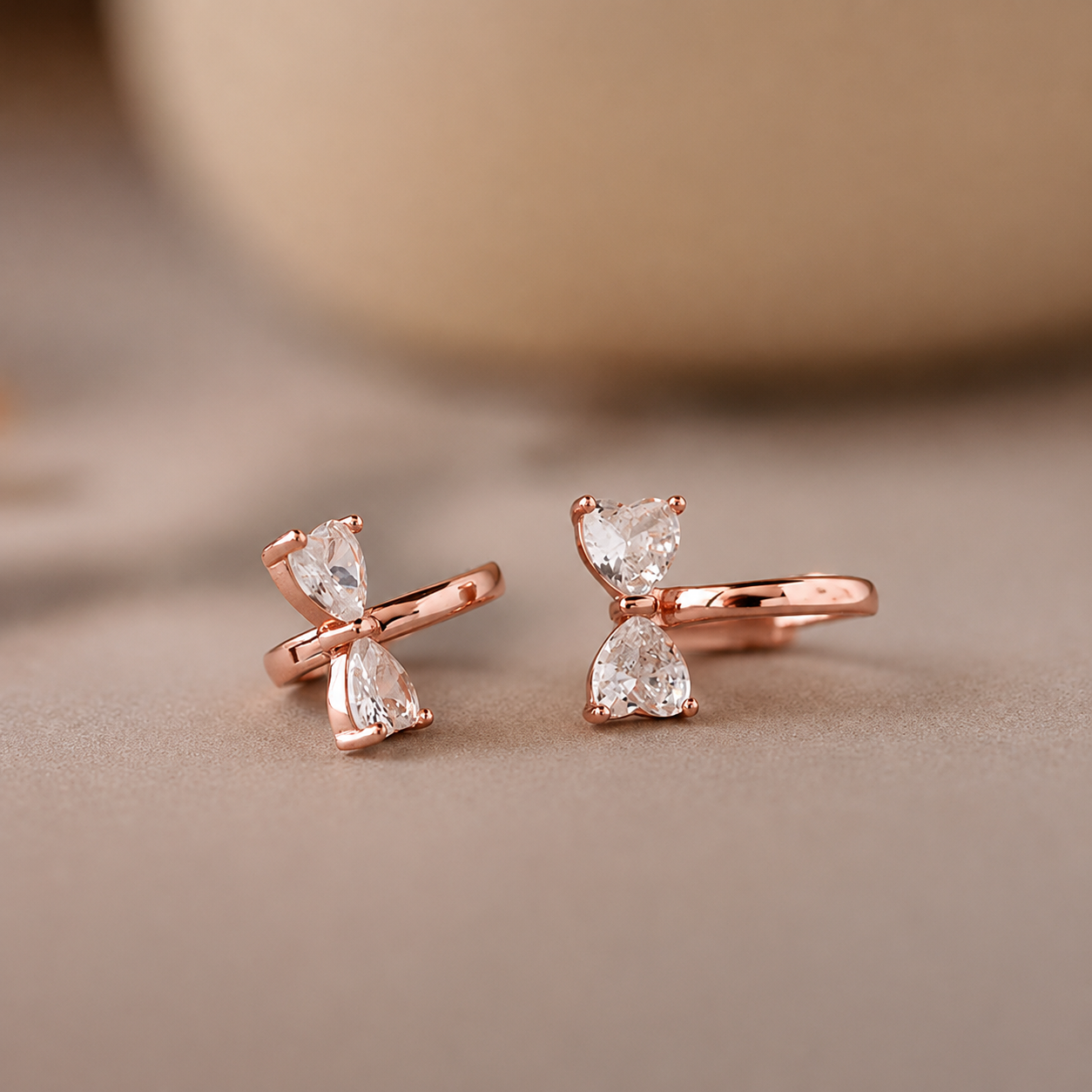 Rose gold earrings with clear gemstones on a beige background