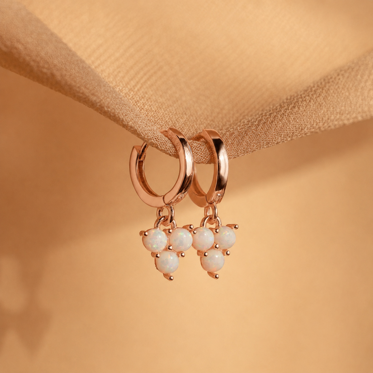 Rose gold hoop earrings with pearl drops on a beige fabric background