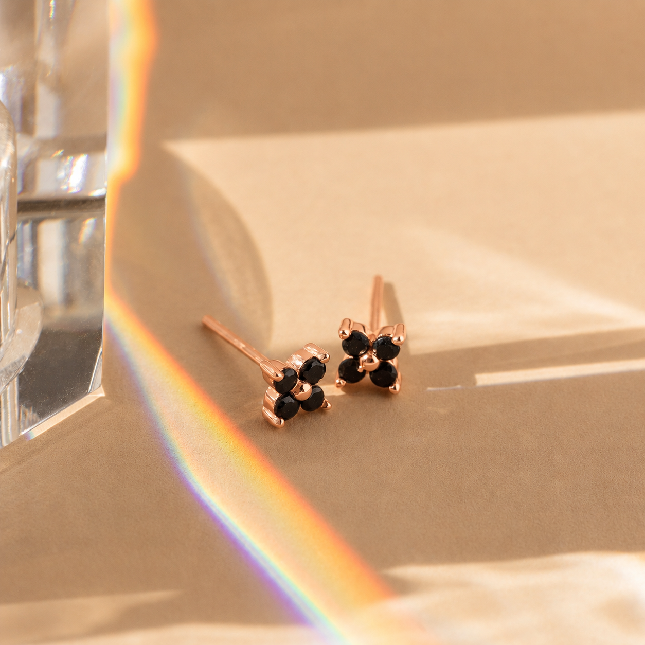 Rose gold earrings with black stones on a reflective surface with a rainbow effect.