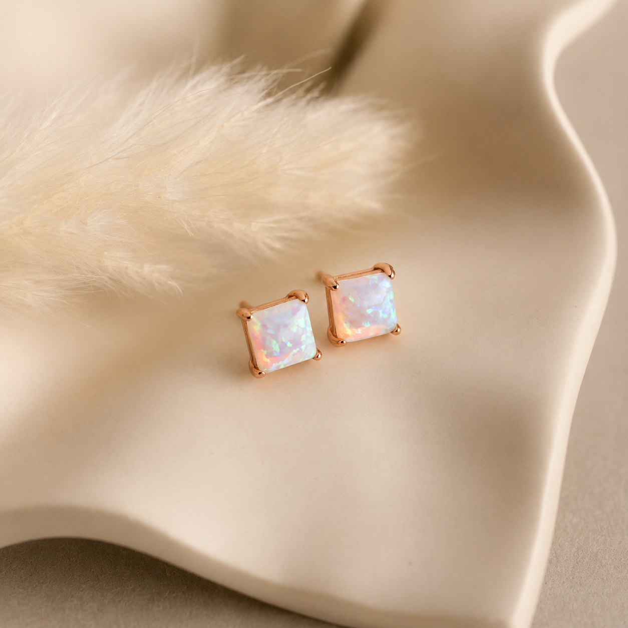 Rose gold square stud earrings on a beige fabric background
