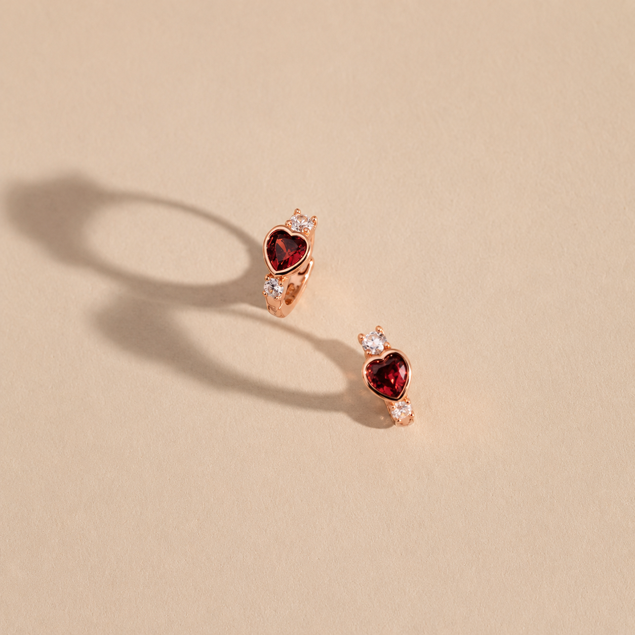 Heart-shaped earrings with red gemstones on a beige background