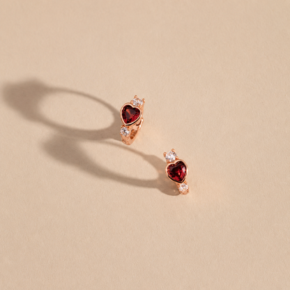 Heart-shaped earrings with red gemstones on a beige background
