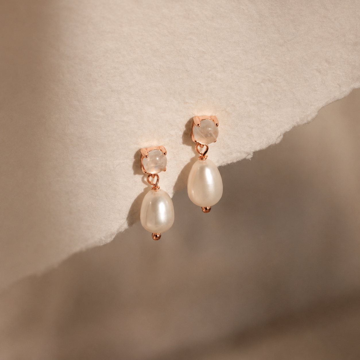 Pearl earrings with rose gold accents on a textured beige background