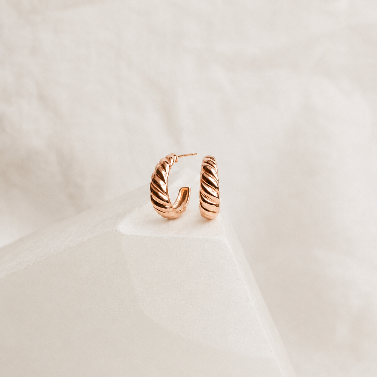 Rose gold hoop earrings on a light beige background