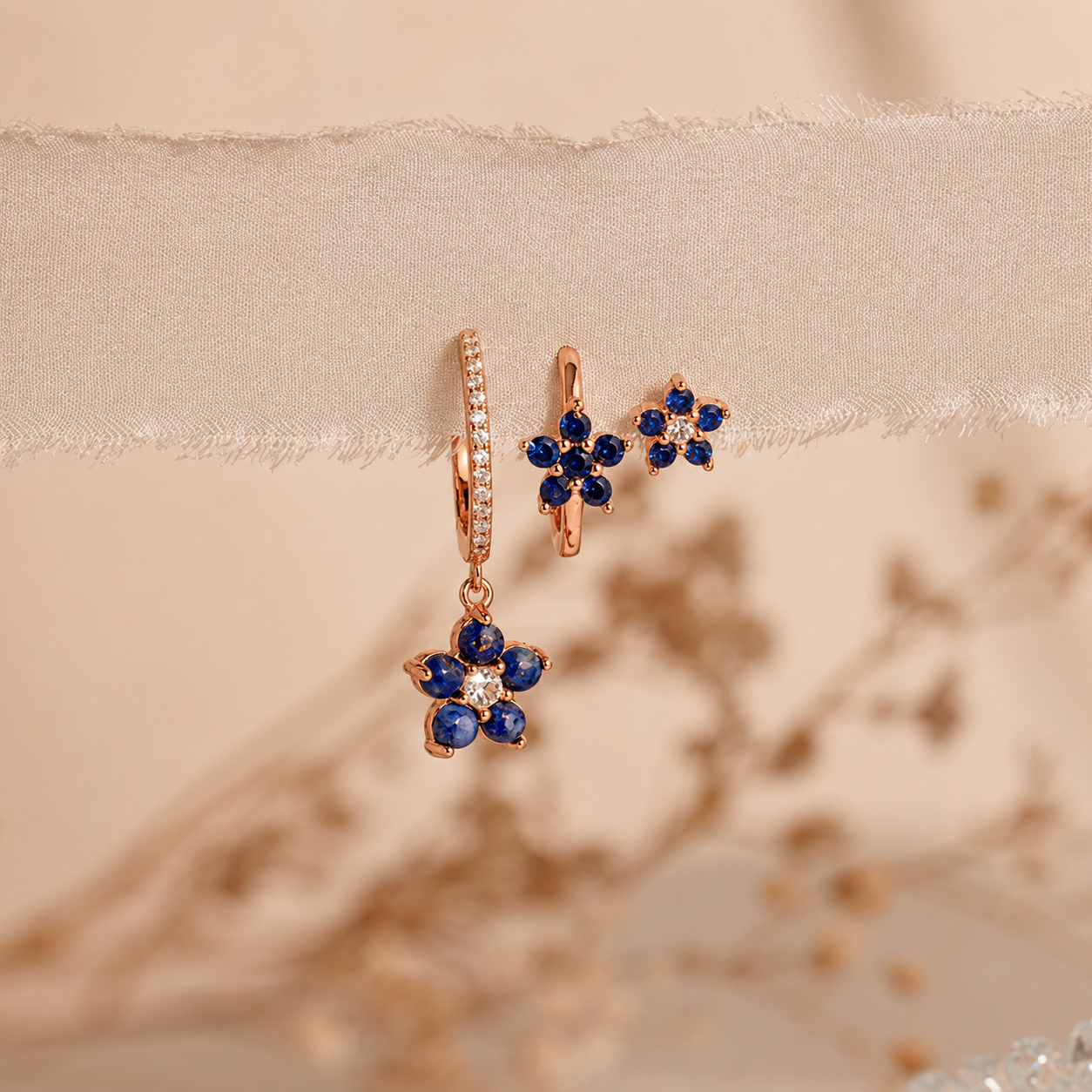 Rose gold earrings with blue gemstones on a beige fabric background