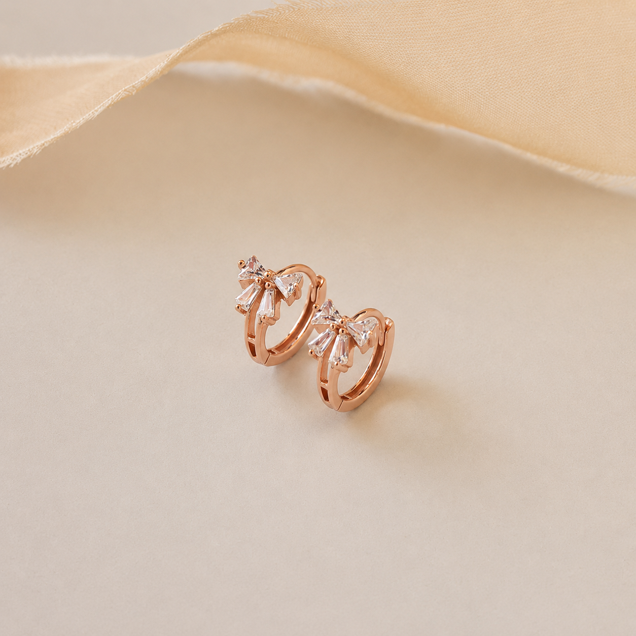 Rose gold earrings with clear gemstones on a beige fabric background