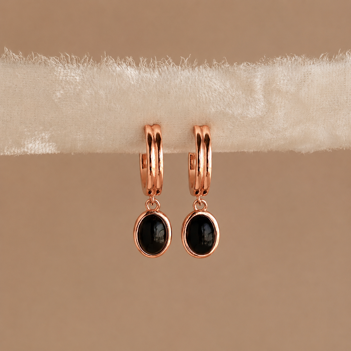Rose gold hoop earrings with black stones on a beige background