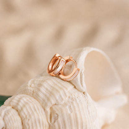 Rose gold hoop earrings on a seashell with a blurred beige background