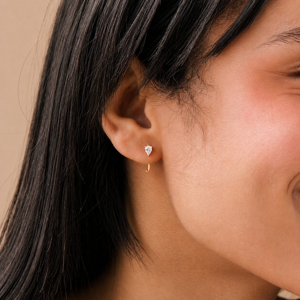 Close-up of a person wearing a pear-shaped earring with a neutral background