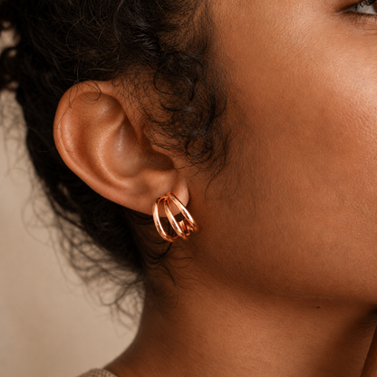 A close-up of a person's ear wearing a pair of rose gold hoop earrings with a twisted, layered design.