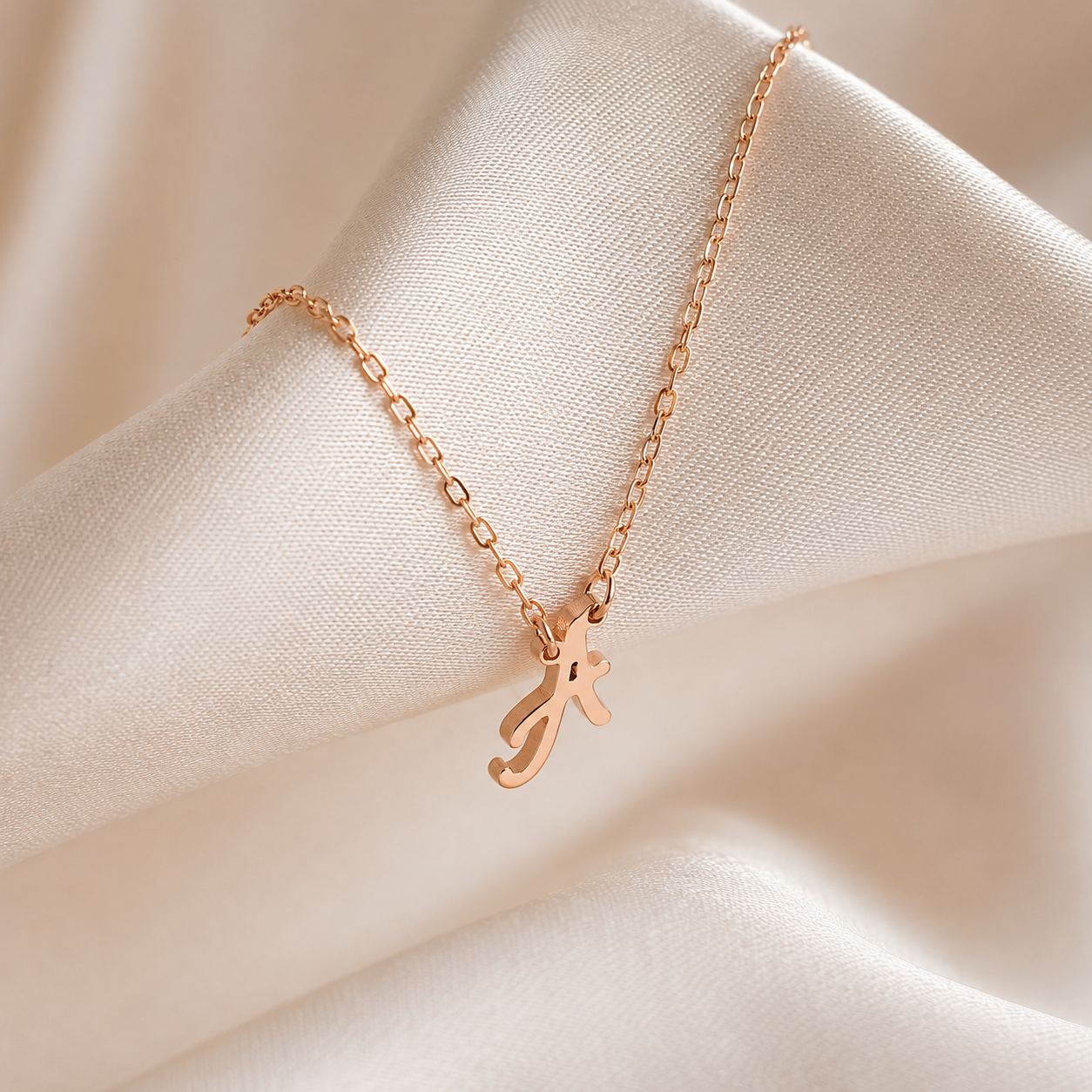 Rose gold necklace with a letter 'J' pendant on a beige fabric background